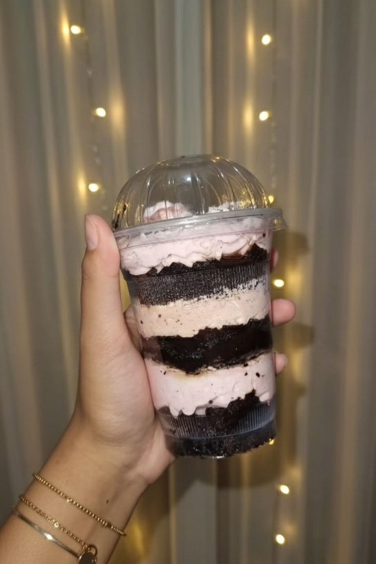 Layered chocolate glass cake with pink cream in a clear dome-lid cup