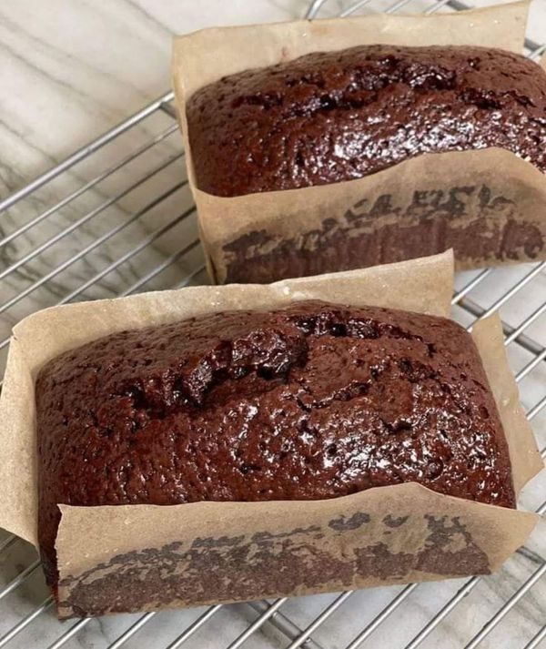 Two freshly baked chocolate loaf cakes in parchment paper on a cooling rack