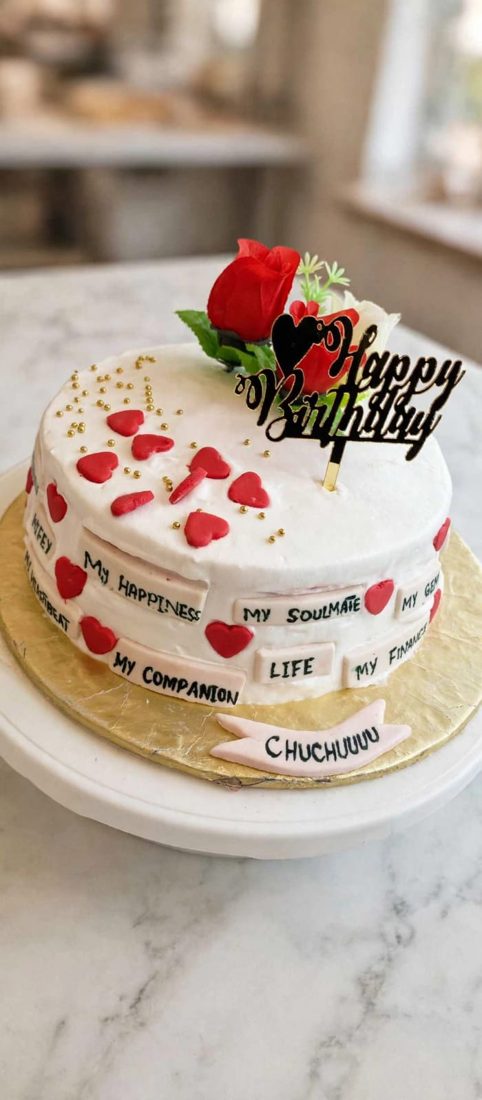 White-frosted anniversary cake with red heart accents and a floral topper