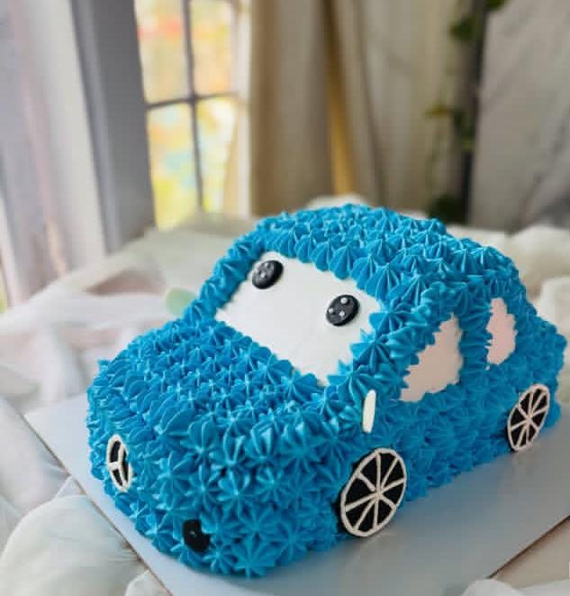 Blue car-shaped cake with piped frosting, dark windows and wheels