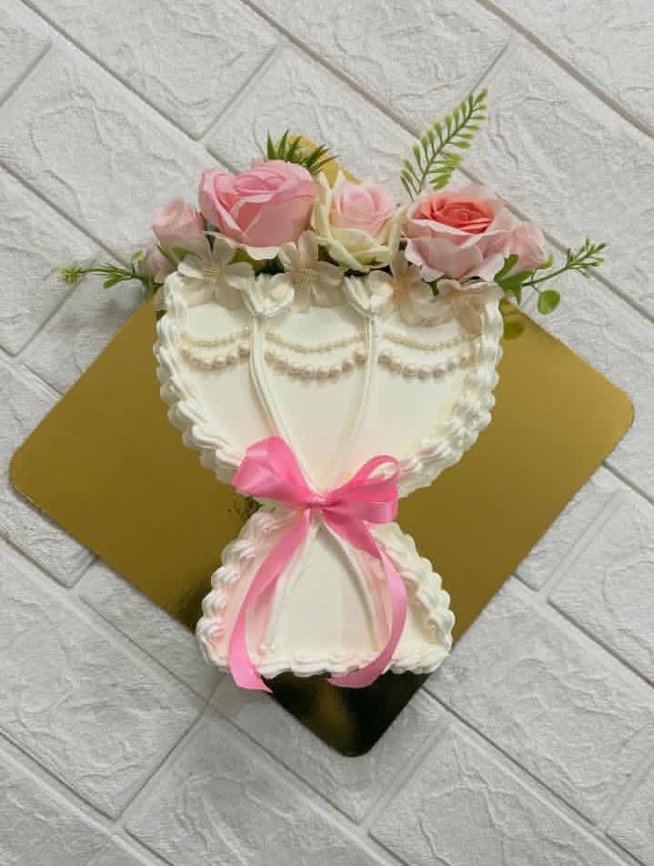 Heart-shaped cake with white frosting, pink roses and green foliage