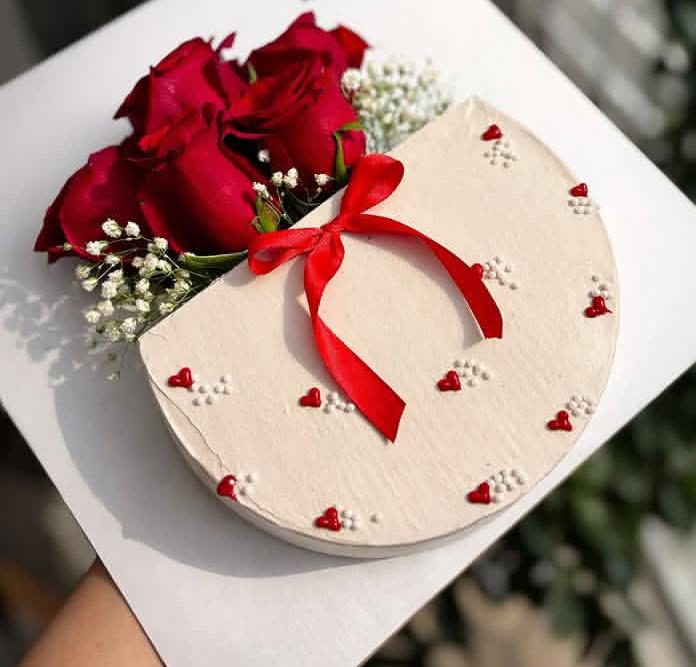 Heart-shaped white cake with a red ribbon, red hearts and roses beside it
