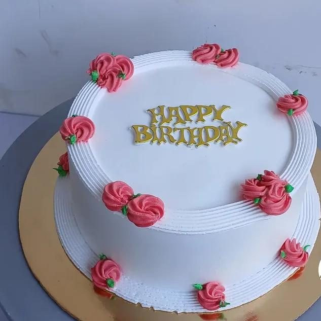 White birthday cake with pink rosettes and a piped border