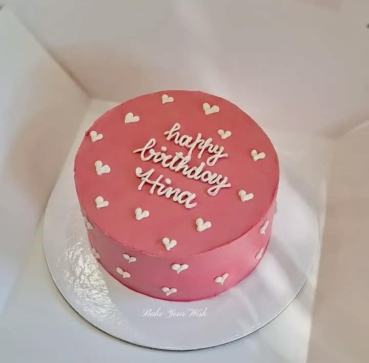 Pink buttercream birthday cake with small white hearts and a handwritten birthday message