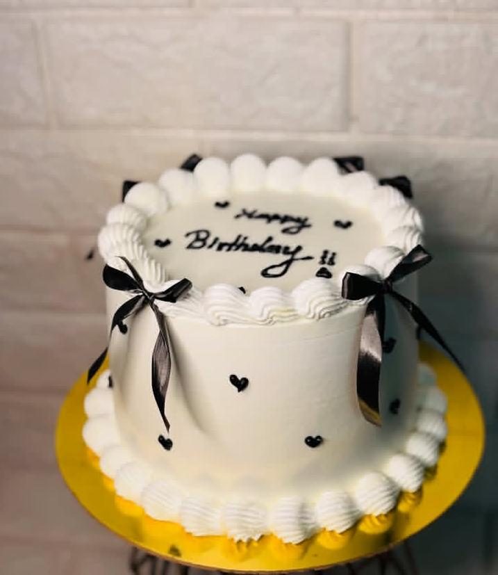 White cake with black ribbon bows, piped borders and hearts