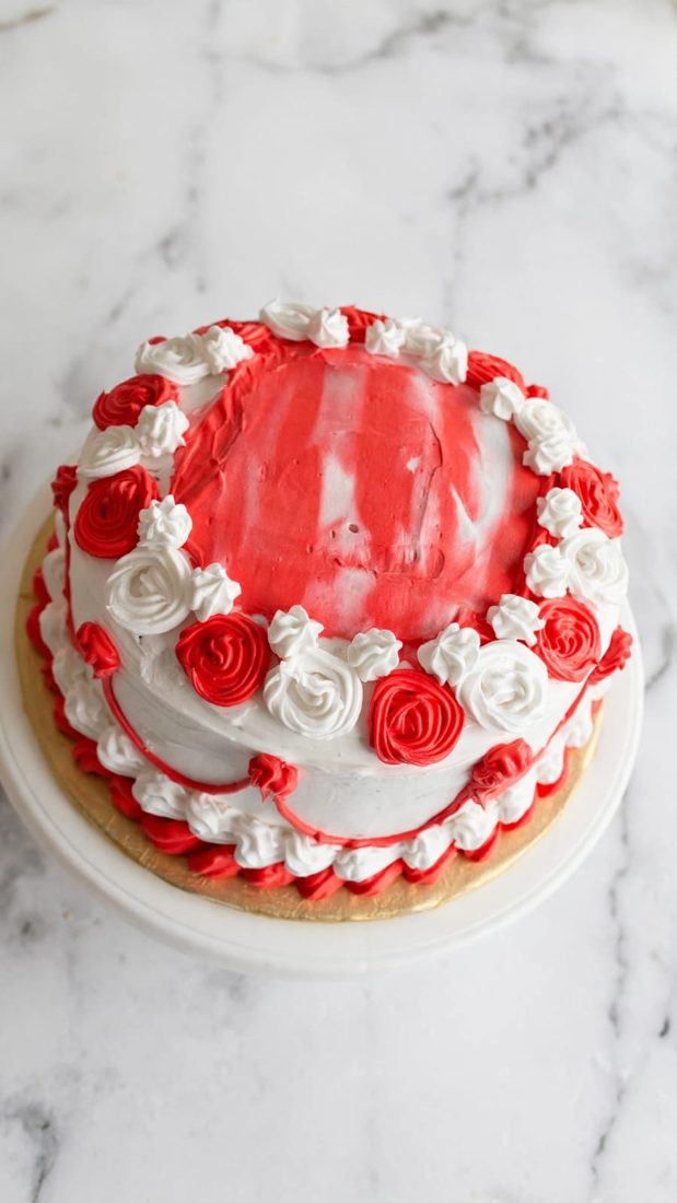 Round vanilla cake with white frosting and red-and-white piped cream rosettes