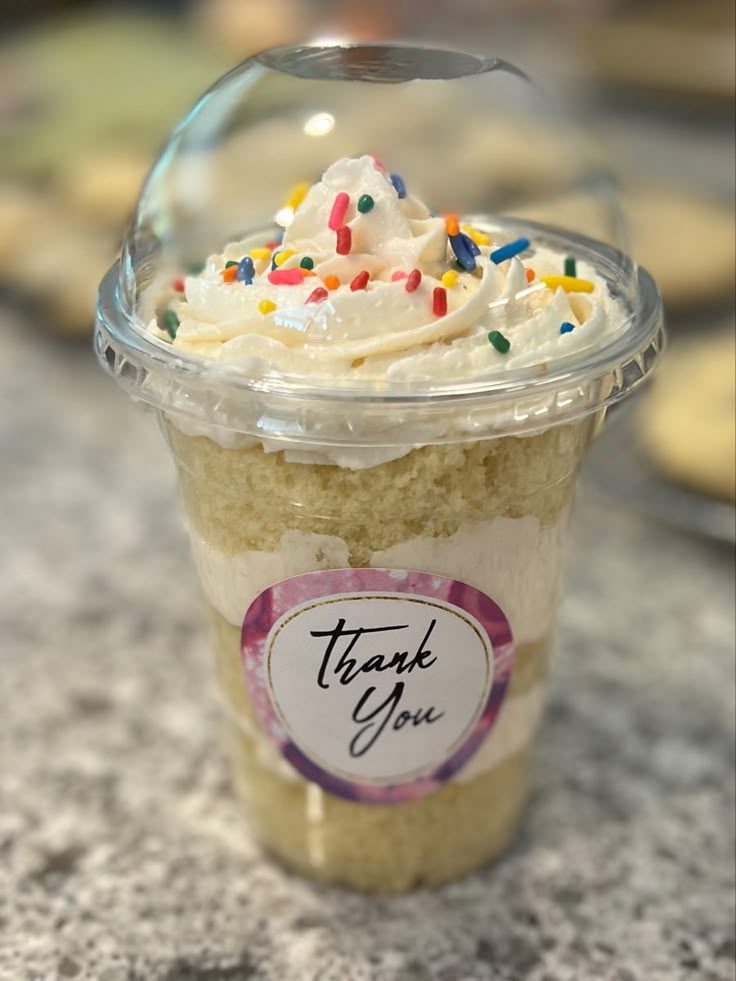 Vanilla glass cake topped with cream and sprinkles in a dome-lid cup with a thank-you sticker